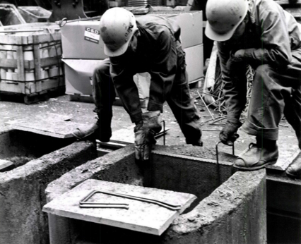 Black-and-white photograph of two steelworkers handling equipment in an industrial work area